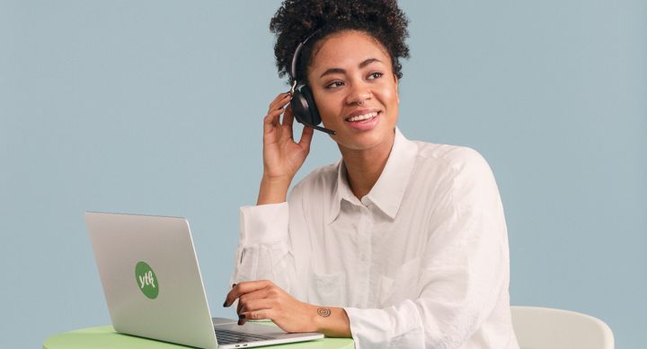 Henkilö istuu pöydän ääressä kannettavan tietokoneen kanssa ja käyttää kuulokkeita.