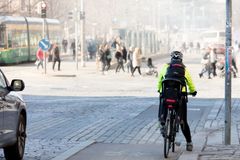 Pyöräilijä seisoo risteyksessä, ja suojatietä pitkin kävelee ihmisjoukko katupölypilven seassa.