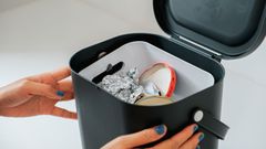 Kuvassa kädet laittavat kierrätysastiaan metalliroskaa, kuten metallisia purkin kansia ja foliota.