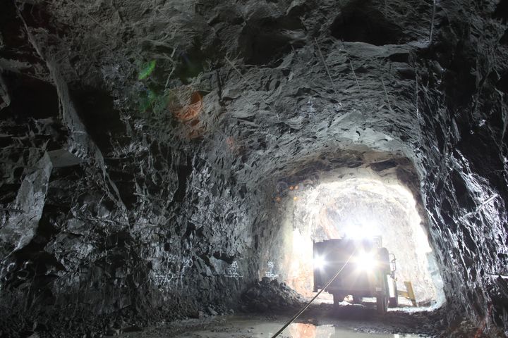 Kuvassa on kallioon louhittu iso tunneli, jossa kulkee kuorma-ajoneuvo. Muuten pimeää, mutta ajoneuvon valot valaisevat.