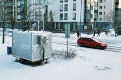 Harmaa mittausasema seisoo kadun varressa.