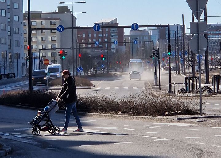 Henkilö kävelee lapsen kanssa kävelytietä pitkin kadulla, jossa näkyy katupölyä.