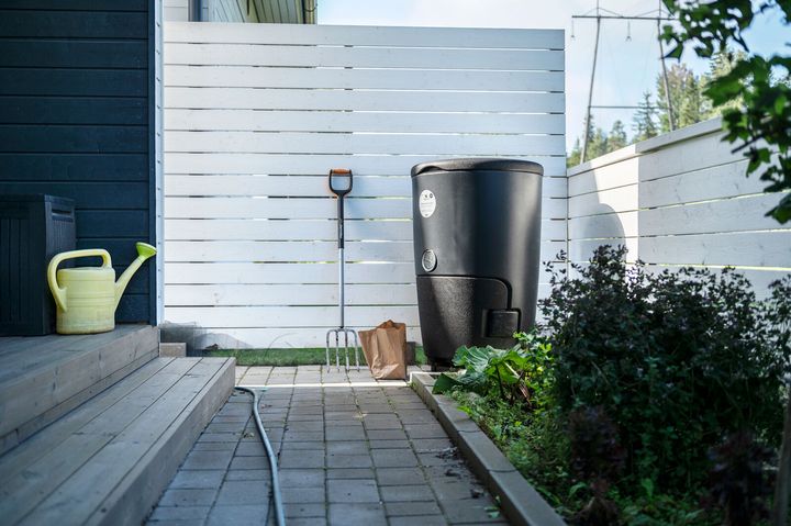 Piha, jossa on valkoinen aita, musta kompostiastia, harava, kastelukannu ja paperikassi.