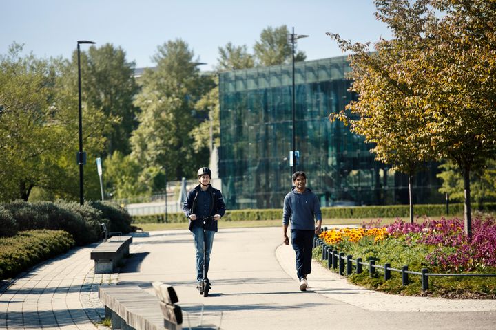 Kuvassa on kevyen liikenteen väylällä sähköpotkulautailija ja jalankulkija.