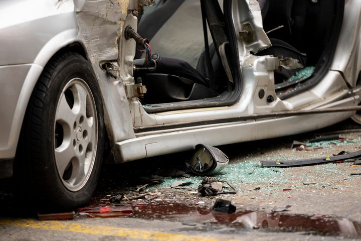 Auto-onnettomuus, jossa henkilöauto on tiellä vaurioituneena, ovi auki. Maassa lasinsirpaleita ja romua.