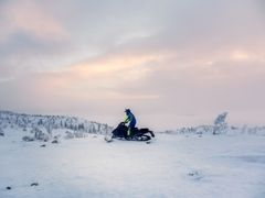 Moottorikelkkailija ajaa lumisessa maisemassa.