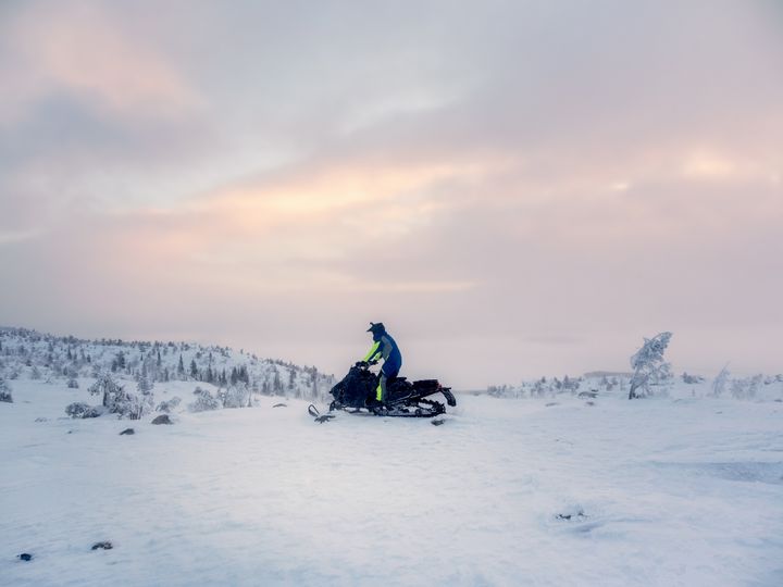 Moottorikelkkailija ajaa lumisessa maisemassa.