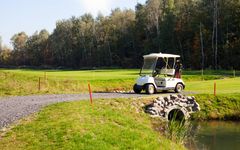 Golfkärry seisoo kapealla hiekkatiellä golfkentän vieressä, taustalla metsä.