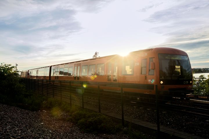 Metrojuna liikenteessä, taustalla paistaa aurinko