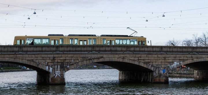 Raitiovaunu ylittämässä Pitkääsiltaa. Raitiovaunun yläpuolella näkyvät ajolangat ja sillan alapuolella on vettä.