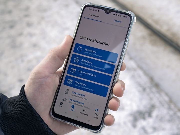Kuvituskuva, henkilöllä puhelin kädessä, HSL-sovelluksesta Osta lippu -näkymä auki.