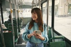 Nainen seisoo raitiovaunussa iloisena puhelin kädessä ja katsoo ulospäin.