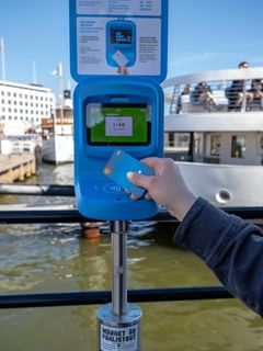 Matkustaja näyttää lauttarannassa maksukorttia lukijalaitteelle ja ostaa HSL:n kertalipun lähimaksulla.