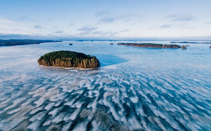 Ilmakuva talvisesta, jään peitossa olevasta järvestä, jossa on metsäisiä saaria.