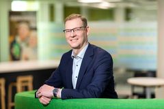 henkilö, joka on pukeutunut pukuun ja seisoo vihreän sohvan edessä modernissa toimistoympäristössä. S-Pankin ekonomisti Janne Ronkanen.