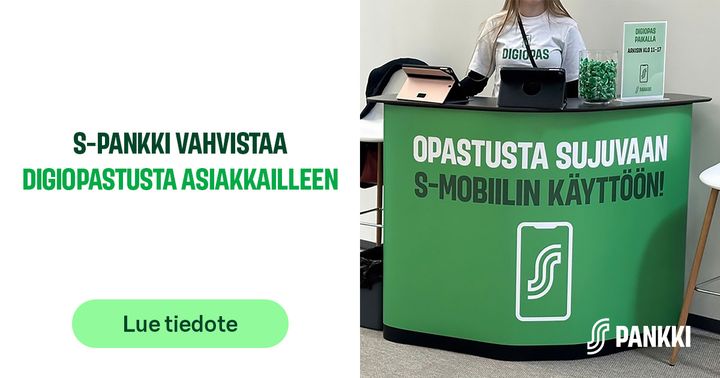 Henkilö seisoo pankin opastuspisteen takana, pöydällä digineuvontaan liittyvä materiaali.