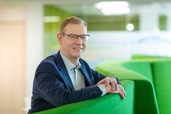 Janne Ronkanen. Henkilö seisoo moderneissa toimistotiloissa nojaten vihreään huonekaluun. Hänellä on silmälasit ja hän hymyilee.