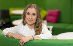 Veera Kosonen, S-Banken. Kvinna i vit tröja sitter på en grön soffa i ett rum med gröna väggar och flerfärgade kuddar.