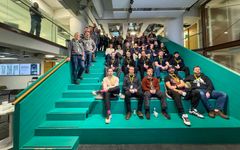 Ryhmä ihmisiä istuu portailla sisätiloissa. He katsovat kameraan ja hymyilevät.