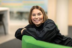 Annemari Airaksinen, S-Pankki, nainen istuu vihreällä sohvalla, hymyilee ja nojaa käsillä selkänojaan.