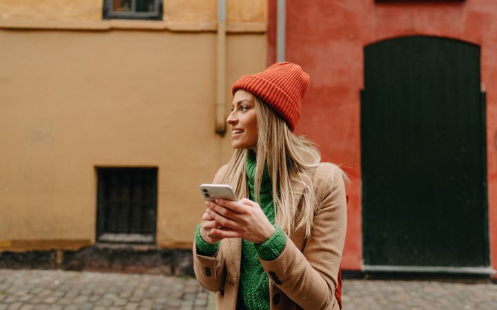 Henkilö pitelee älypuhelinta kädessään ulkona värikkäiden rakennusten edustalla.