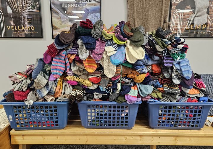 Kolme sinistä koria täynnä erivärisiä neulottuja villasukkia.