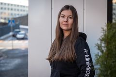 Nainen seisoo ulkona, pukeutunut mustaan huppariin.