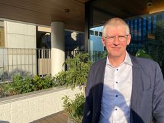 Per Hansen, jolla on silmälasit ja puku, seisoo terassilla aurinkoisella säällä.