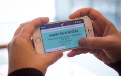Henkilö pitää älypuhelinta kädessään; näytöllä on teksti "Kaikki tai ei mitään."