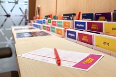 Pöydällä on Veikkaus-lomakkeita ja punainen kynä. Taustalla värikkäitä mainoksia peleistä, kuten Lotto ja Eurojackpot.