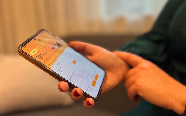 Henkilö käyttää älypuhelinta, jossa on auki sovellus oranssisävyisellä taustalla.