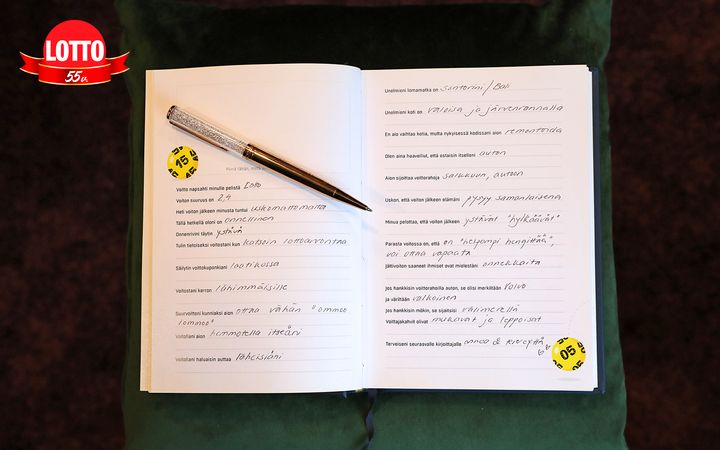 Avoin kirja, jonka sivuilla on kirjoitettu tekstiä ja joiden päällä on kynä. Kirjaan on liimattu kaksi keltaista lappua, joissa on numerot 75 ja 50. Yläkulmassa on Lotto-logo.