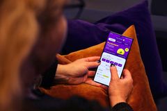 Henkilö käyttää älypuhelinta istuen sohvalla, näytöllä näkyy sovellus lilalla taustalla.