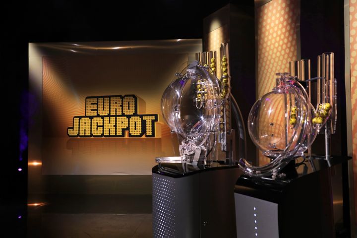 Eurojackpot-studion sisustus Helsingin Pasilassa, taustalla iso logo ja edessä lottoarvontakoneet.