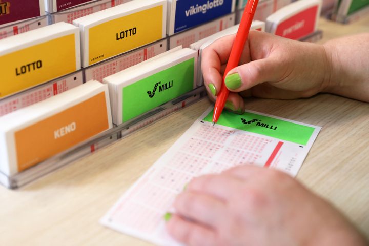 Henkilö pitelee älypuhelinta, jossa on auki Milli-pelisovellus. Vieressä kahvikuppi.