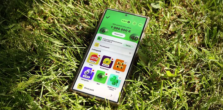 Älypuhelin, jossa on auki lotto-sovellus, makaa vihreällä ruohikolla.