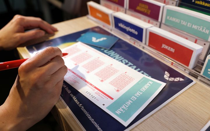 Henkilö täyttämässä Kaikki tai ei mitään -pelikuponkia kynällä.