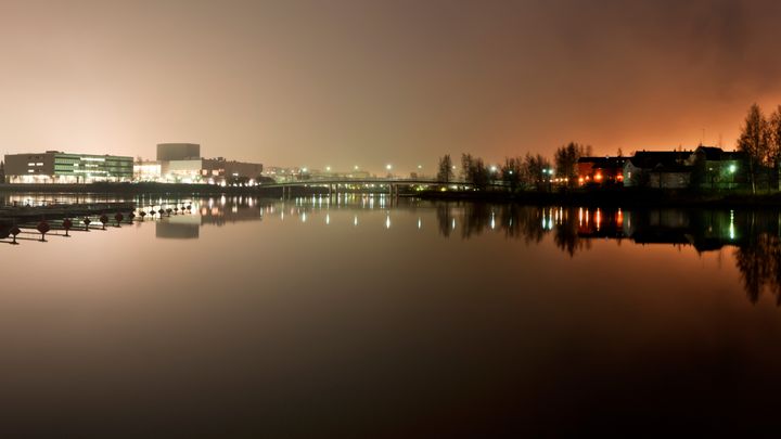 Joki, silta ja kaupungin rakennuksia iltavalaistuksessa.
