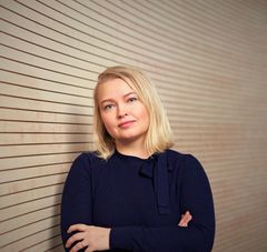 Vaalea henkilö mustassa paidassa vaaleanruskean seinän edustalla.