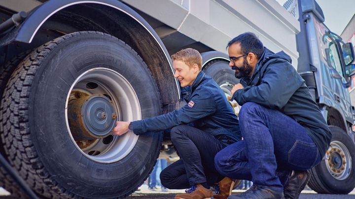 Kaksi henkilöä kumartuneena tutkimaan suuren rekan rengasta.