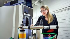 Kuvassa henkilö seisoo NMR-spektroskoppilaitteen vieressä laboratoriossa.