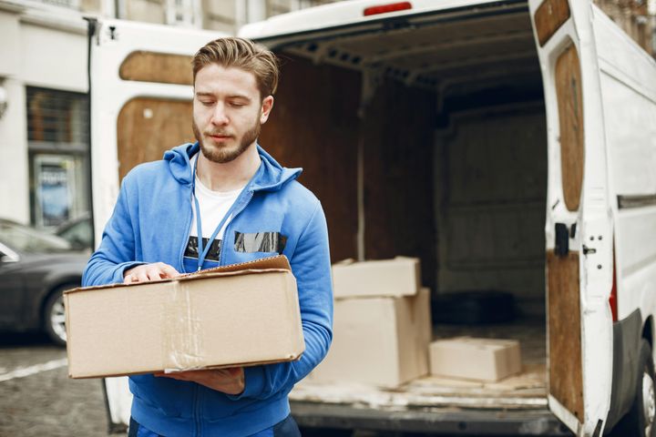mies kantaa laatikkoa pakettiautosta