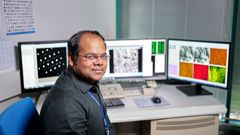 Mies istuu tietokoneen ääressä laboratoriossa, näytöillä näkyy teräksen tutkimukseen liittyviä kuvia ja tietoja.