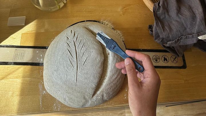 Käsi pitelee terää ja tekee viiltoa kuvioituun leipätaikinaan.