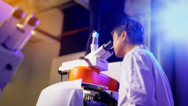 RamanProSeq-hankkeen tavoitteena on kehittää uudenlainen optinen teknologia yksittäisten proteiinimolekyylien sekvensointiin. Kuvassa apulaisprofessori Jianan Huang ja Raman-mikroskooppi. Kuva: Oulun yliopisto / Mikko Törmänen.