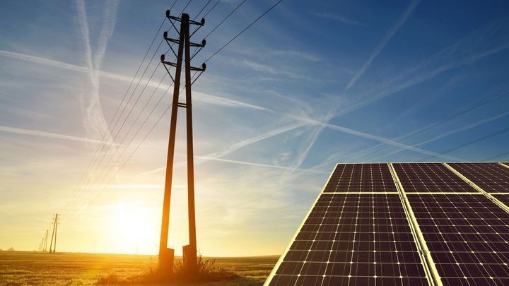 Sähkölinja aurinkoisessa maisemassa, etualalla aurinkopaneeli.