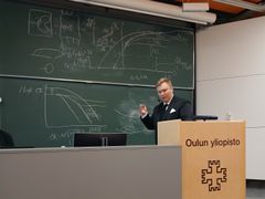 Mies pitämässä esitelmää yliopiston luokkahuoneessa liitutaulun edessä.