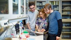 Kolme tutkijaa katsoo kannettavaa tietokonetta laboratoriossa.