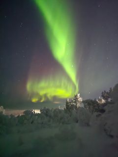 Revontulet loistavat vihreänä ja purppurana taivaalla lumisen maiseman yllä Ukko-Luostolla.