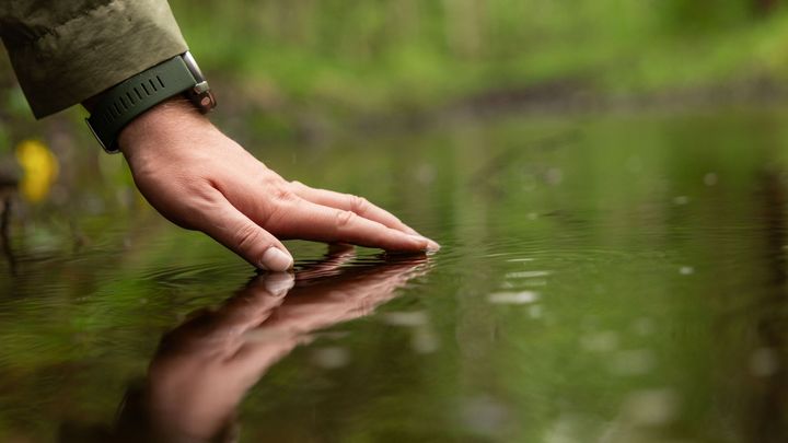 Käsi koskettaa veden pintaa luonnon keskellä.
